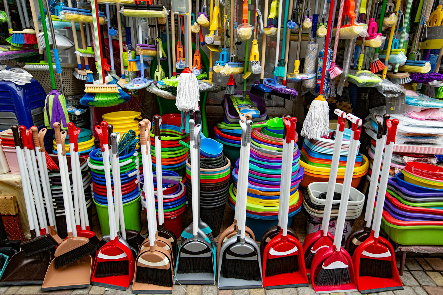 Brightly colored brooms and cleaning supplies arranged in a market setting.
